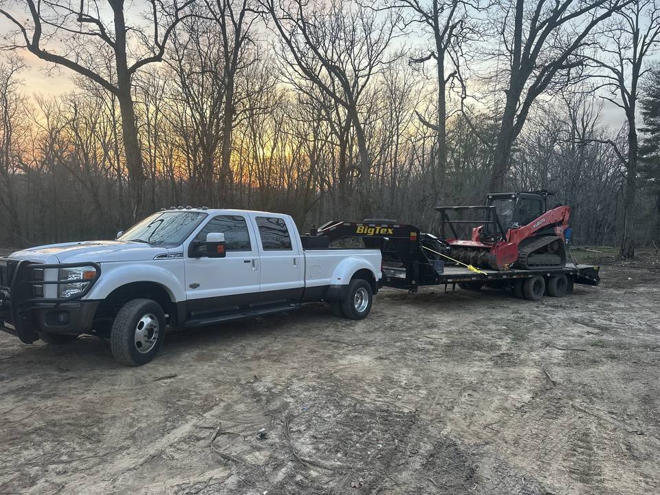 Truck, trailer and track loader on a job site at dusk